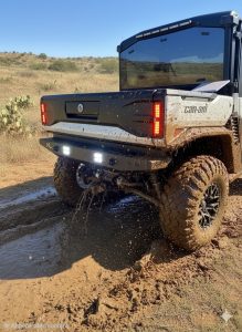 Can-Am Defender HD11 rear bumper with LED lights and integrated camera relocation housing installed in off-road mud